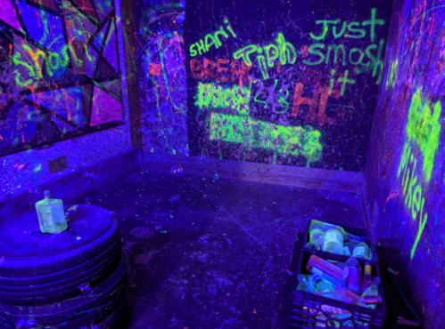 A dimly lit room with glowing graffiti on the walls and a crate of colorful items in the corner.