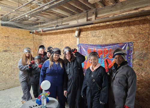 A group of women in work gear and helmets pose together in a decorated room, celebrating an event.