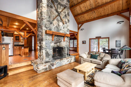 Cozy living area with a stone fireplace, wooden beams, and comfortable seating in a rustic cabin setting.