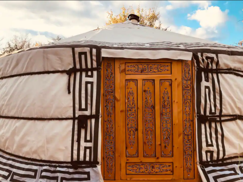 A traditional yurt with a decorative wooden door and intricate patterns on the exterior, set against a blue sky.