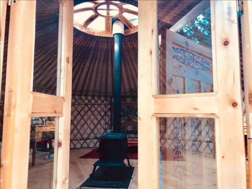 Interior view of a yurt featuring a central wood stove and decorative walls, with a skylight above.
