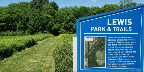 Sign for Lewis Park & Trails with a path through greenery, highlighting outdoor activities like biking and running.