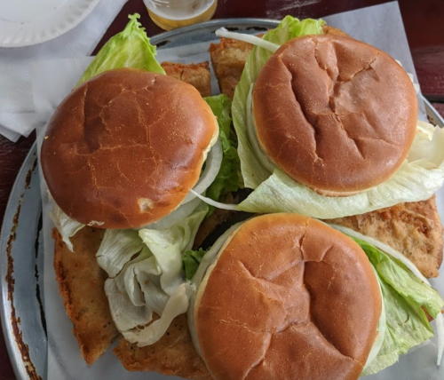 Three sandwich buns with lettuce on a platter, resting on a bed of crispy bread.