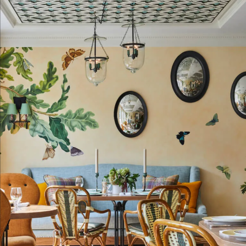 A cozy restaurant interior featuring a mural of leaves and butterflies, elegant mirrors, and stylish seating.
