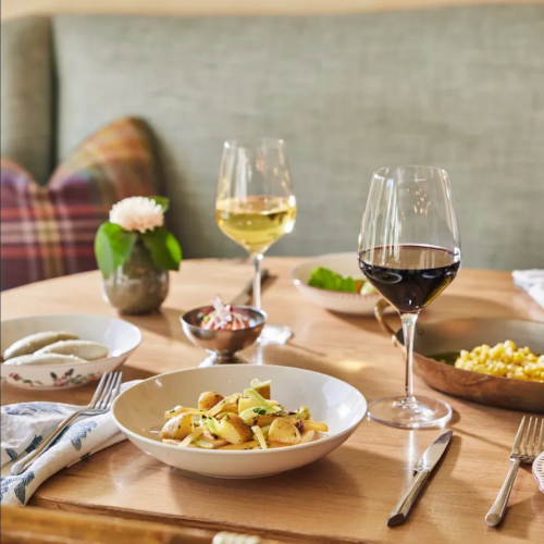 A dining table set with a bowl of pasta, wine glasses, and various side dishes, surrounded by a cozy atmosphere.