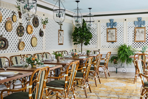 A beautifully decorated dining room with wooden tables, elegant chairs, and floral centerpieces against a lattice wall.