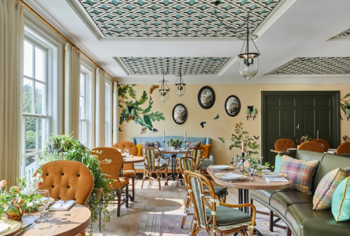 Brightly lit dining room with patterned ceiling, floral decor, and elegant wooden furniture. Cozy and inviting atmosphere.