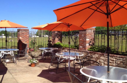 Outdoor patio with orange umbrellas, tables, and a brick wall, set against a clear blue sky.
