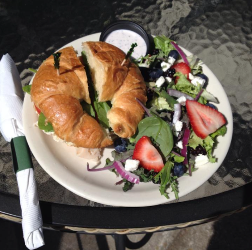 A croissant sandwich with greens, served with a side salad of mixed greens, strawberries, and feta cheese.