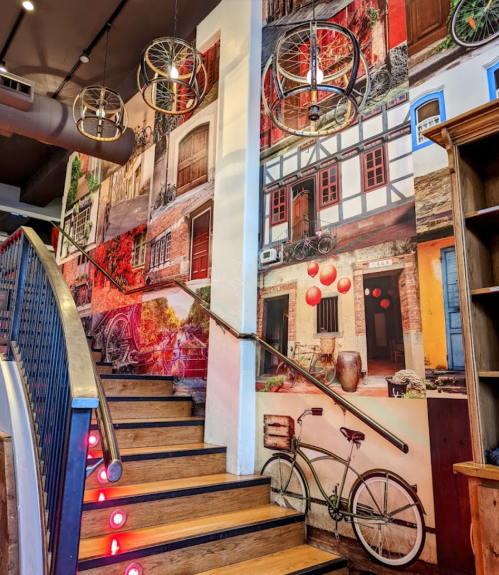 Staircase with wooden steps, adorned with a vibrant mural of buildings and bicycles on the walls.