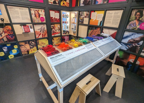 A colorful display of craft materials in a creative space, with stools and informative panels on the walls.