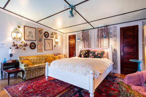 Cozy bedroom featuring a white bed, vintage decor, floral patterns, and a green sofa against a patterned wall.