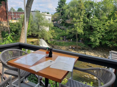 A scenic view from a restaurant balcony overlooking a waterfall and lush greenery, with a table set for dining.