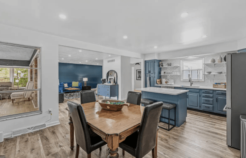 A modern kitchen and dining area with a wooden table, blue cabinets, and bright lighting.