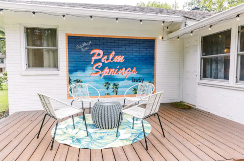 A cozy outdoor seating area with a "Palm Springs Indy" mural, surrounded by string lights and a tropical rug.