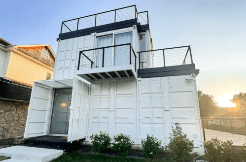 A modern two-story house made from shipping containers, featuring a rooftop deck and a minimalist design.