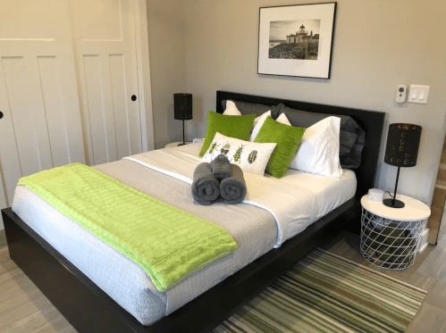A modern bedroom featuring a large bed with green and gray accents, decorative pillows, and stylish lamps.