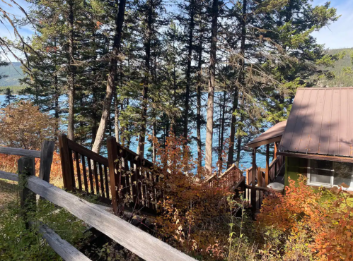 A wooden staircase leads down through trees to a lake, with autumn foliage and a cabin visible nearby.