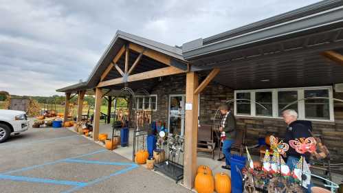 A rustic storefront decorated with pumpkins and autumn decor, with two people browsing outside.