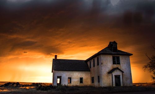 An old, abandoned house silhouetted against a dramatic sunset with dark clouds.