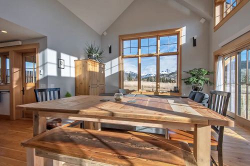 Bright dining area with a wooden table, chairs, and large windows showcasing a mountain view. Natural light floods the space.