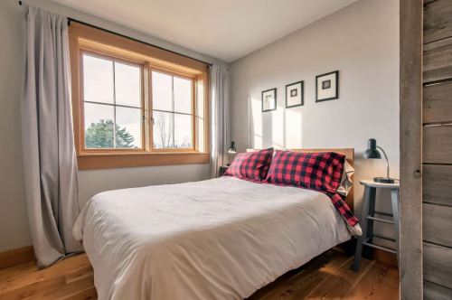 Cozy bedroom with a plaid bedspread, large window, and minimalist decor featuring framed art on the wall.