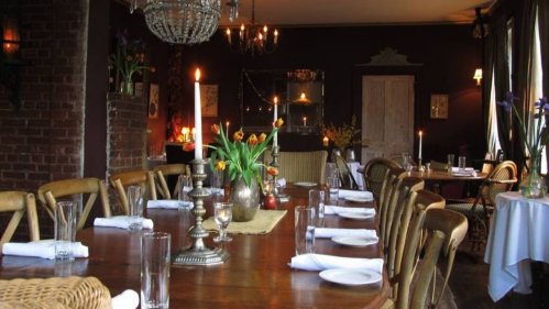Cozy restaurant interior with a wooden table, candles, flowers, and elegant decor, creating a warm ambiance.