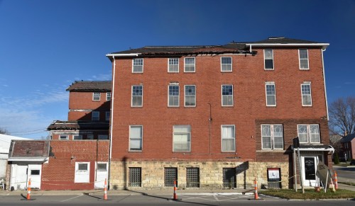 Abandoned red brick building with multiple stories, showing signs of decay and damage, under a clear blue sky.