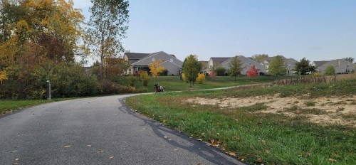 A winding path leads through a park with colorful autumn trees and houses in the background under a clear sky.
