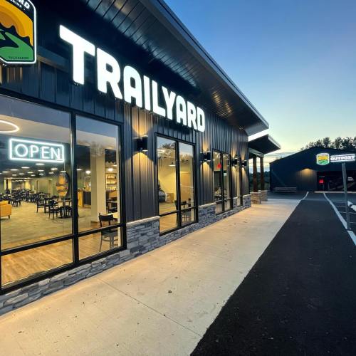 Exterior of a modern building with "TRAILYARD" sign, large windows, and an "OPEN" sign, during twilight.