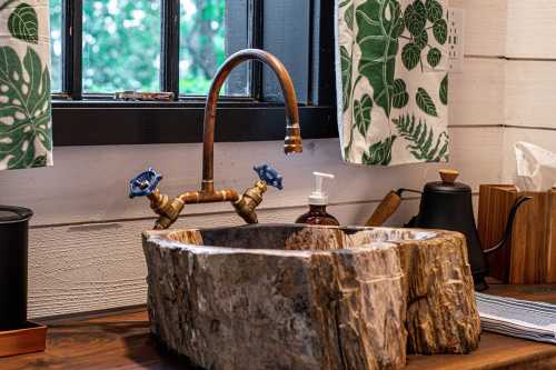 A rustic wooden sink with a unique shape, featuring a stylish faucet and blue handles, set in a cozy kitchen.