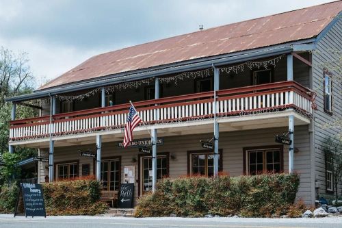 A two-story building with a red roof, American flag, and a sign for a restaurant, surrounded by greenery.