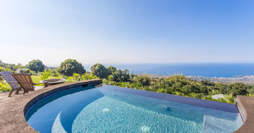 A serene infinity pool overlooking a lush landscape and ocean view under a clear blue sky.