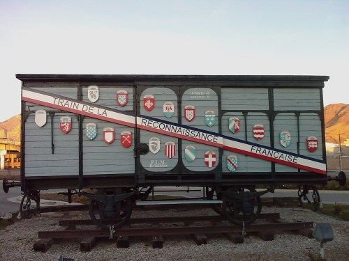 A historic train car decorated with various shields, displayed outdoors against a mountainous backdrop.