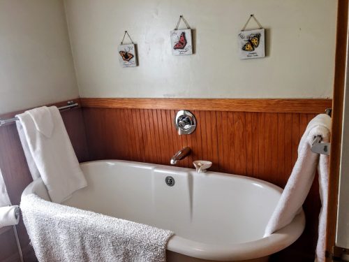 A cozy bathroom featuring a white bathtub, wooden paneling, and butterfly art on the wall. Soft towels are neatly arranged.
