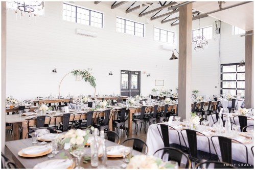 Elegant event space with long wooden tables, floral centerpieces, and large windows letting in natural light.
