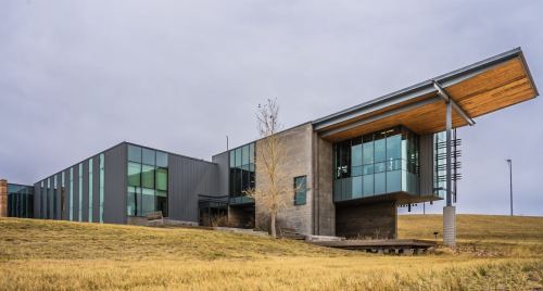 Modern building with large glass windows and a distinctive overhanging roof, set against a grassy landscape.
