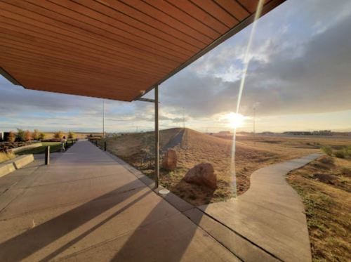 A pathway curves around a grassy hill under a wooden overhang, with a bright sunrise in the background.