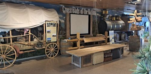 Exhibit featuring a wooden wagon, barrels, and historical artifacts in a museum setting.