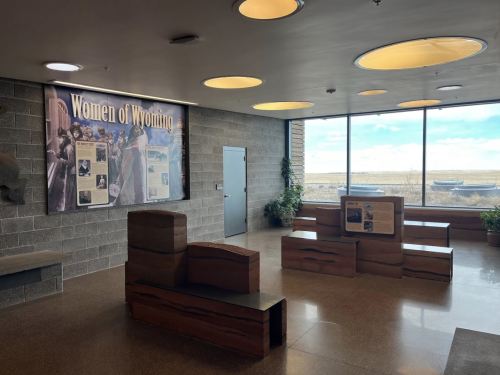 Interior view of a space featuring a "Women of Wyoming" exhibit, with seating and large windows showing a landscape.