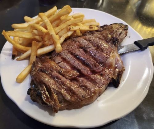A grilled steak with grill marks served on a plate alongside a portion of golden French fries.