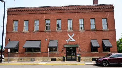 A brick building with large windows and awnings, featuring a modern logo on the front.
