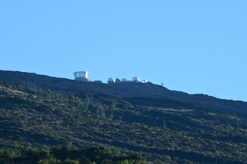 A distant view of observatories on a mountain ridge against a clear blue sky.