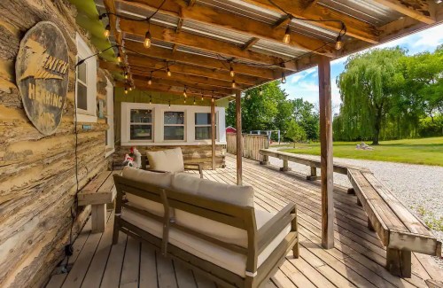Cozy outdoor seating area with string lights, wooden deck, and green landscape in the background.