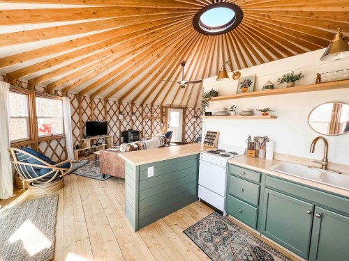 Cozy yurt interior with wooden beams, a kitchen area, living space, and large windows for natural light.