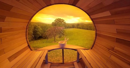 A cozy wooden interior with a view of a golden sunset over a green landscape and trees.