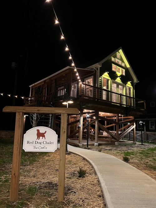 A cozy chalet at night, illuminated by string lights, with a sign reading "Red Dog Chalet" in front.