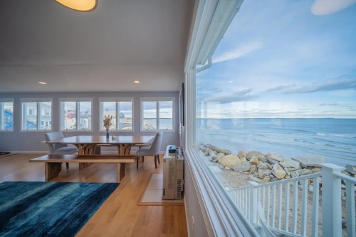 Bright dining area with a wooden table, large windows overlooking the ocean, and a view of the beach and sky.