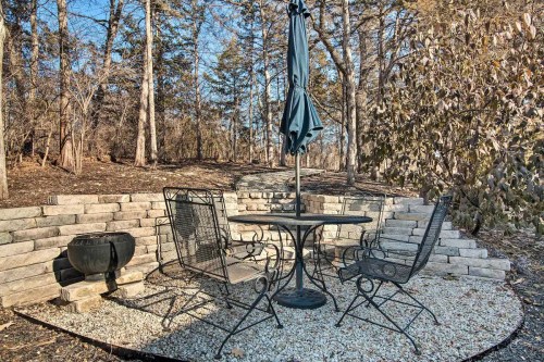 A cozy outdoor seating area with a table, chairs, and an umbrella, surrounded by trees and stone walls.