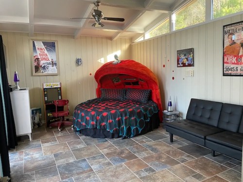A cozy bedroom featuring a round bed with a red canopy, black and red bedding, and a modern black sofa.